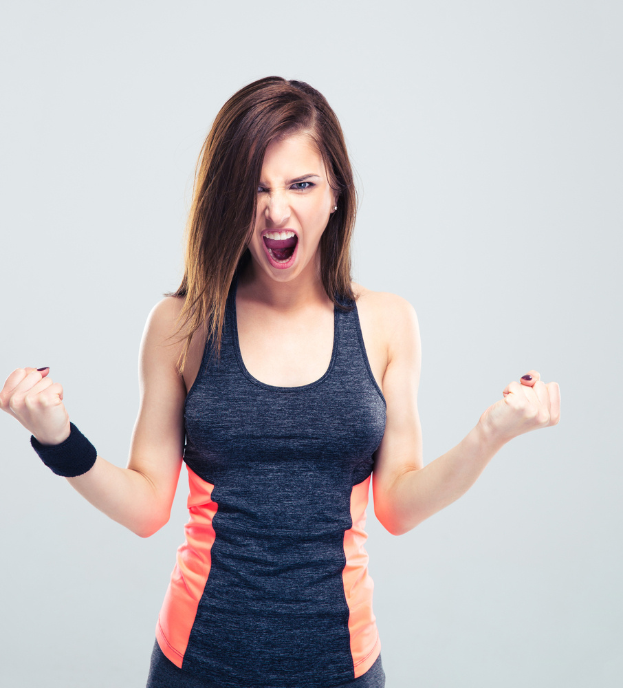Excited young fitness woman shouting on gray background and looking at camera